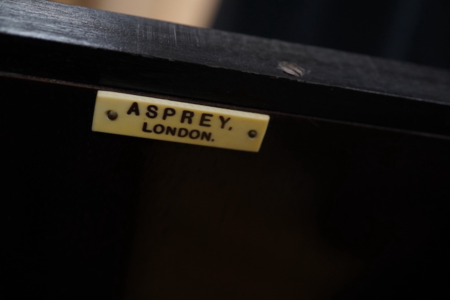 Asprey of London, a cushion-moulded walnut decanter wall cabinet, chromolithograph enclosing four cut glass decanters and six shot glasses, 57cm high, 37.5cm wide. Condition - good.